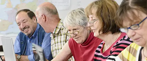 Das Bild zeigt Senioren bei der Arbeit an verschiedenen Laptops in einer Reihe sitzend